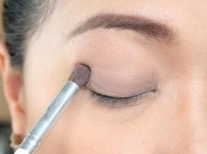 girl applies eyeshadow primer with a brush on her eye lid