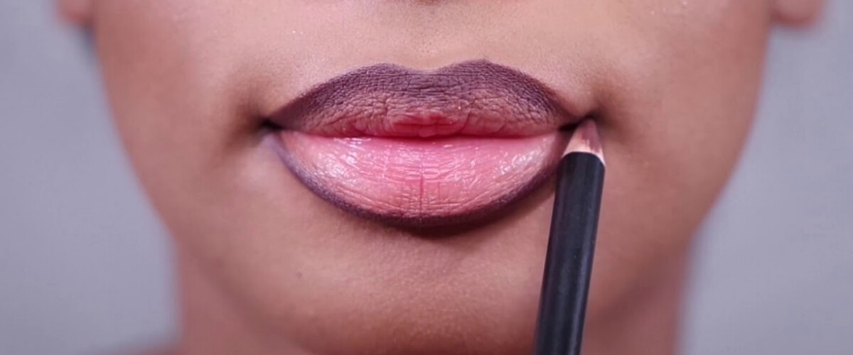 Woman applies dark lip pencil to contour her lips. Plum color