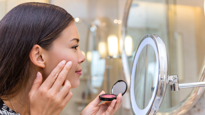 woman applying cream blush into a mirror