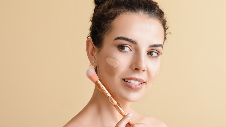 woman holding brush to her face with foundation on her cheek