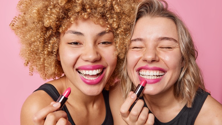 two women happy and applying lipstick